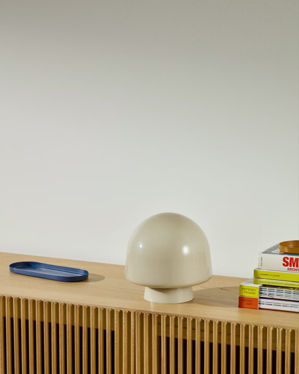 Lámpara de mesa Reig de cristal gris sobre una cómoda de madera y libros decorativos