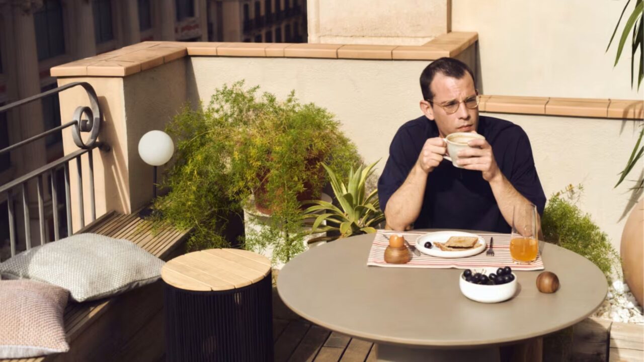 Hombre desayunando en terraza con mesa redonda, café, tostadas y zumo.