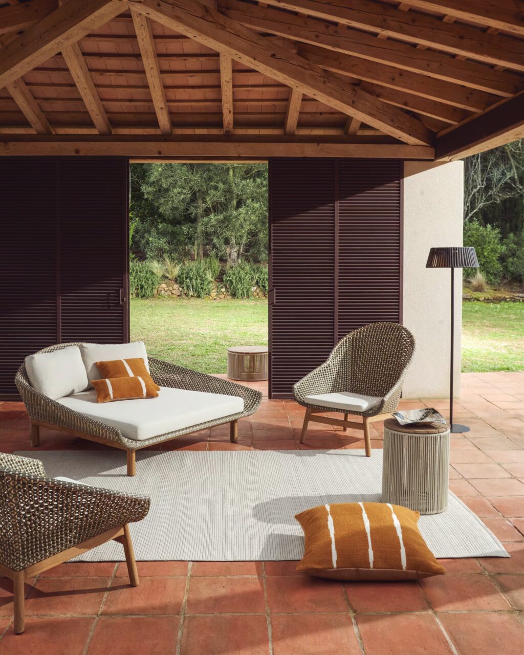 Porche de madera con muebles de exterior de ratán y cojines en tonos neutros.